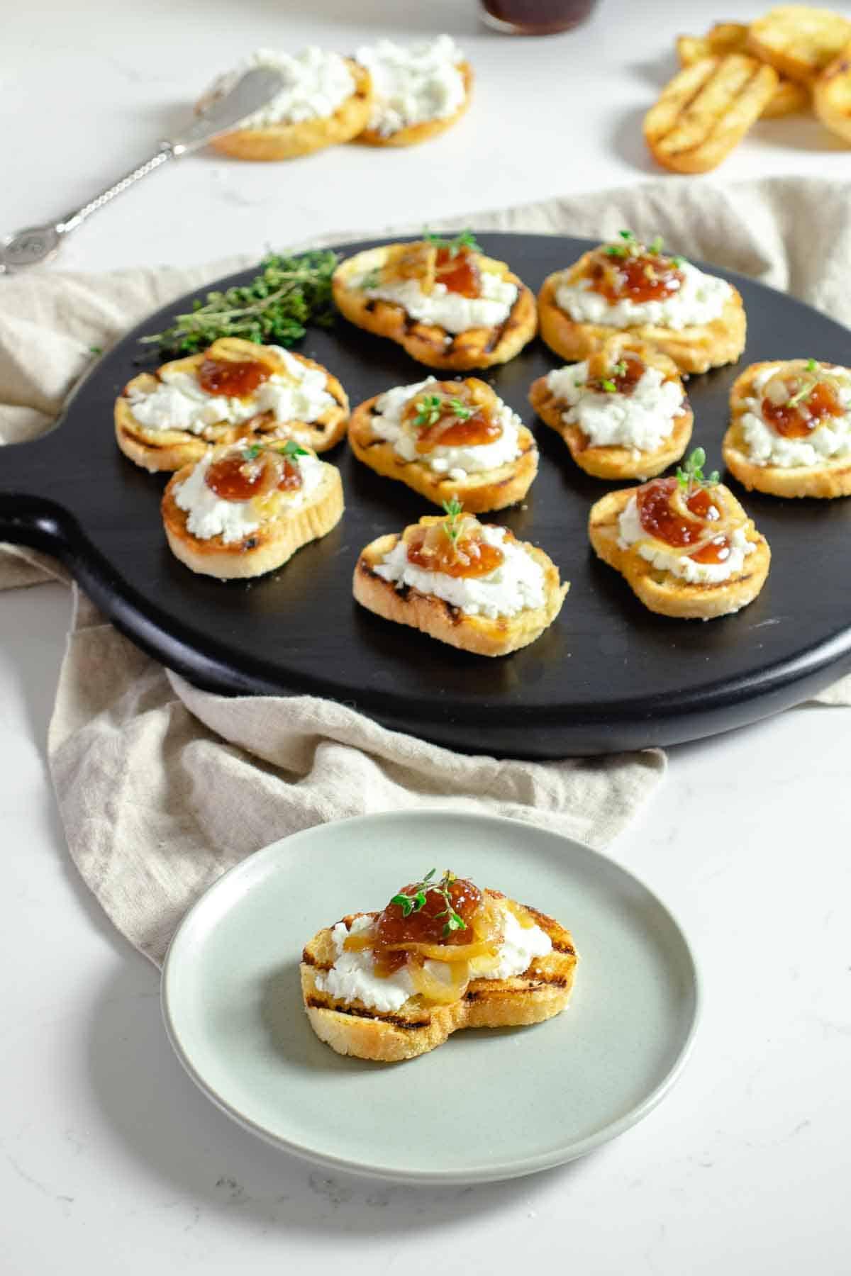 A person smiling while holding a plate of goat cheese and fig jam crostini