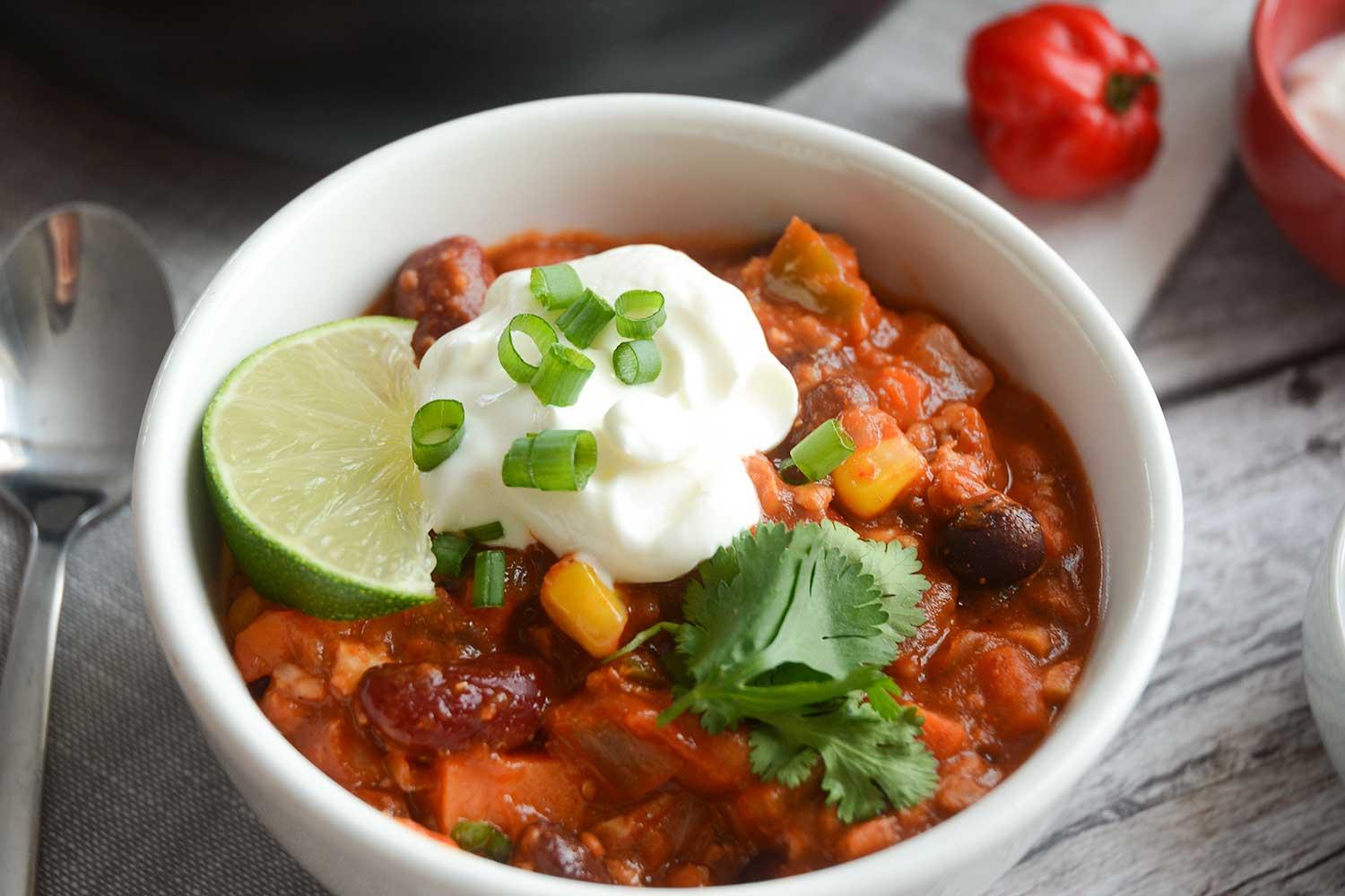 a bowl of vegan chili with walnuts, garnished with fresh cilantro and a dollop of vegan sour cream