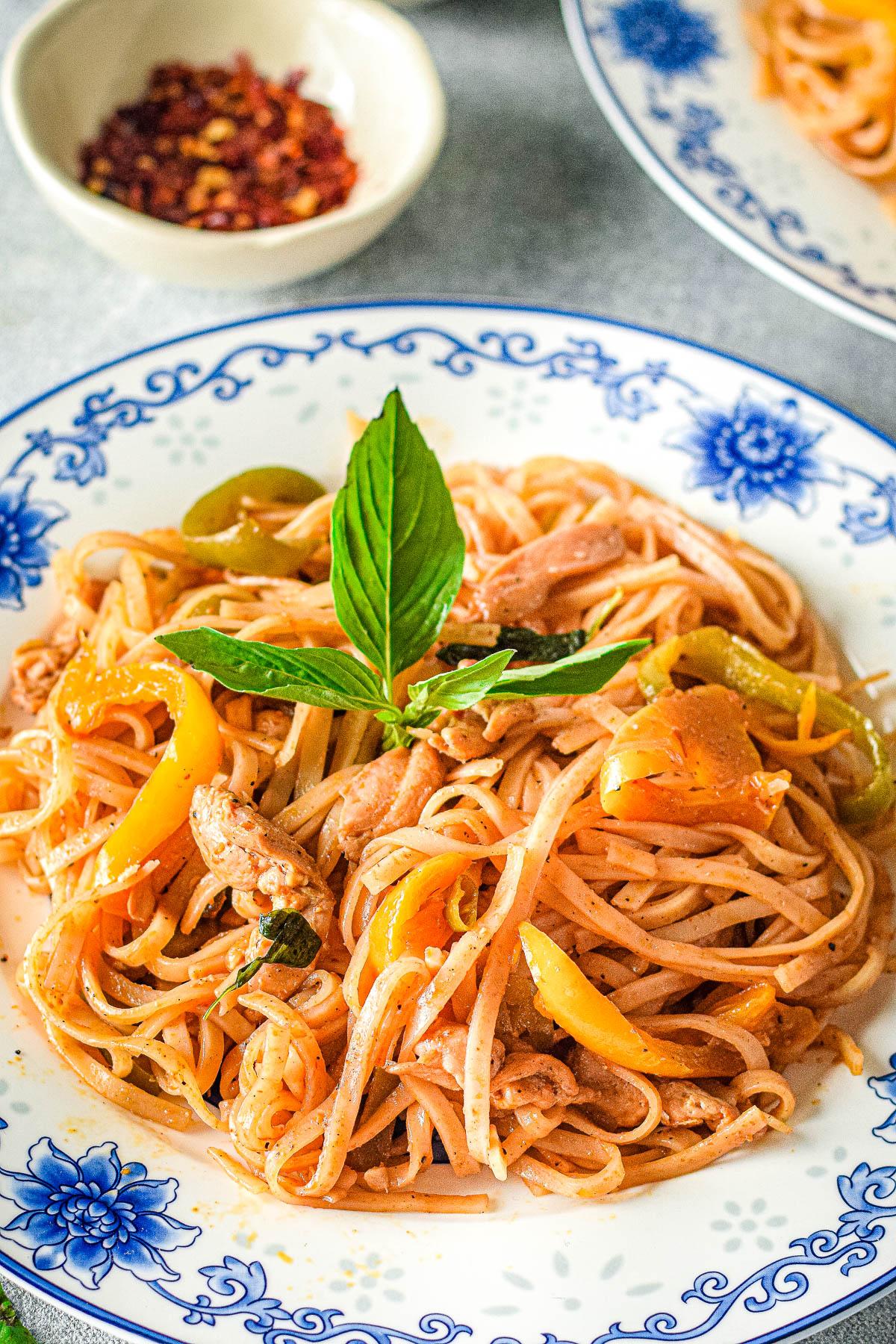 a plate of drunken noodles chicken stir-fry garnished with fresh basil