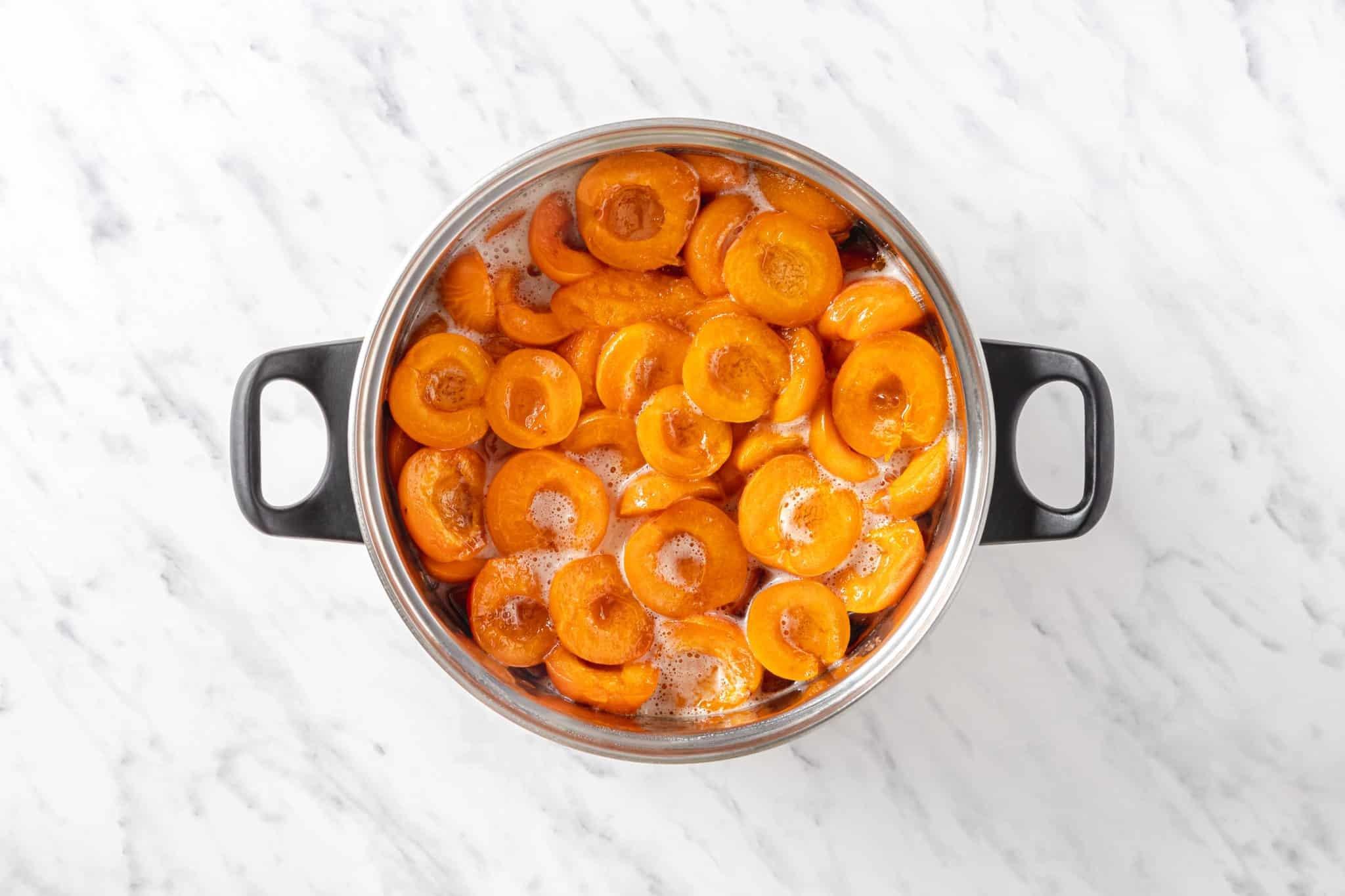 Overhead shot of apricot jam being stirred into a bowl with a spoon, with apricots in the background