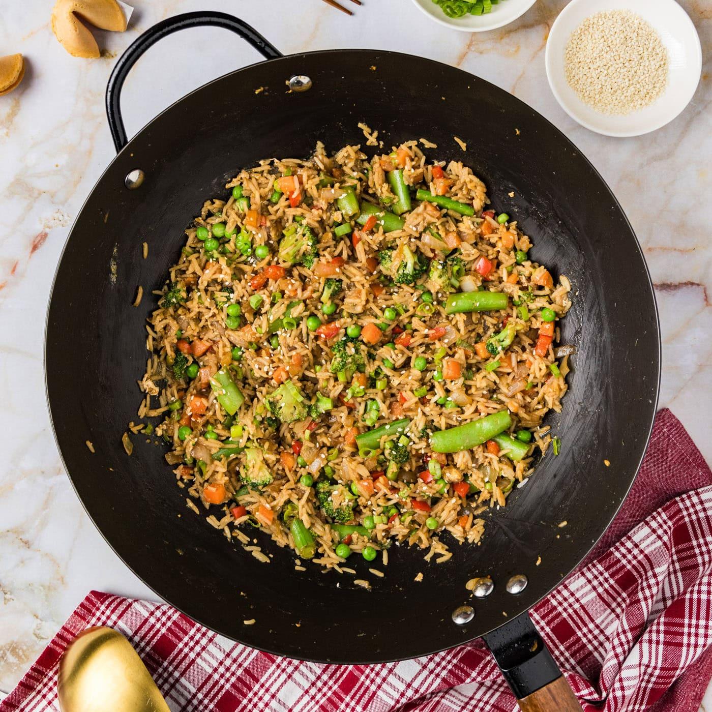 aerial view of the vegetable fried rice being stir-fried in a large wok with various colorful vegetables and seasonings