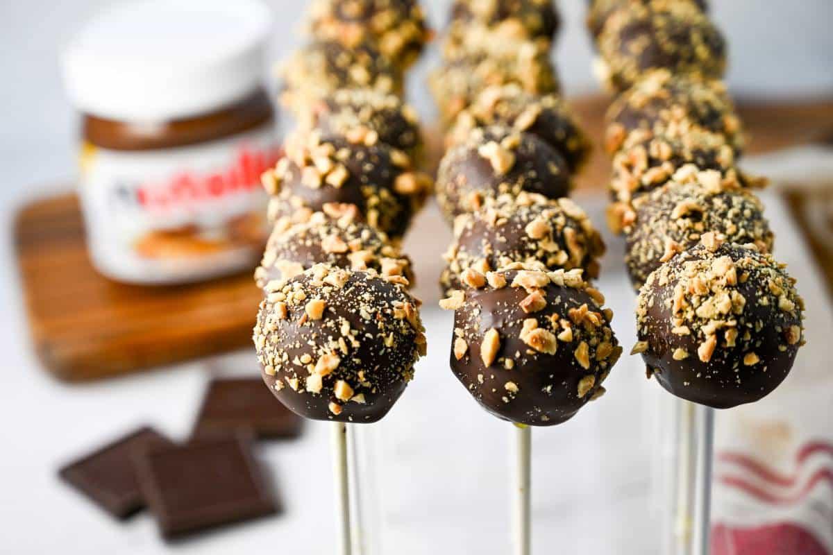 the process of dipping cake pops into melted chocolate and covering them with hazelnuts