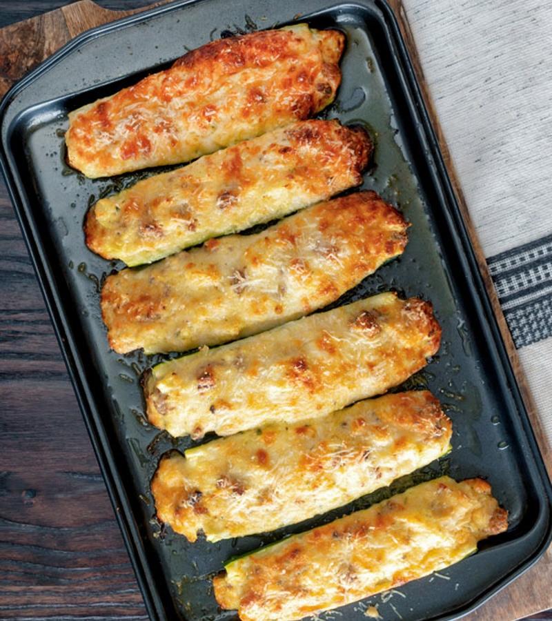 A close-up shot of a slice of zucchini and sausage bake being lifted from the baking dish, showing the layers of zucchini, sausage, cheese, and breadcrumbs.