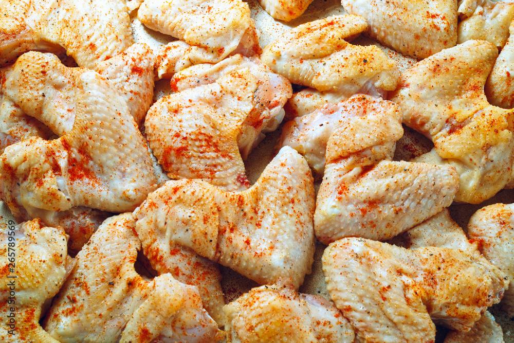 close up of raw chicken wings being seasoned with spices