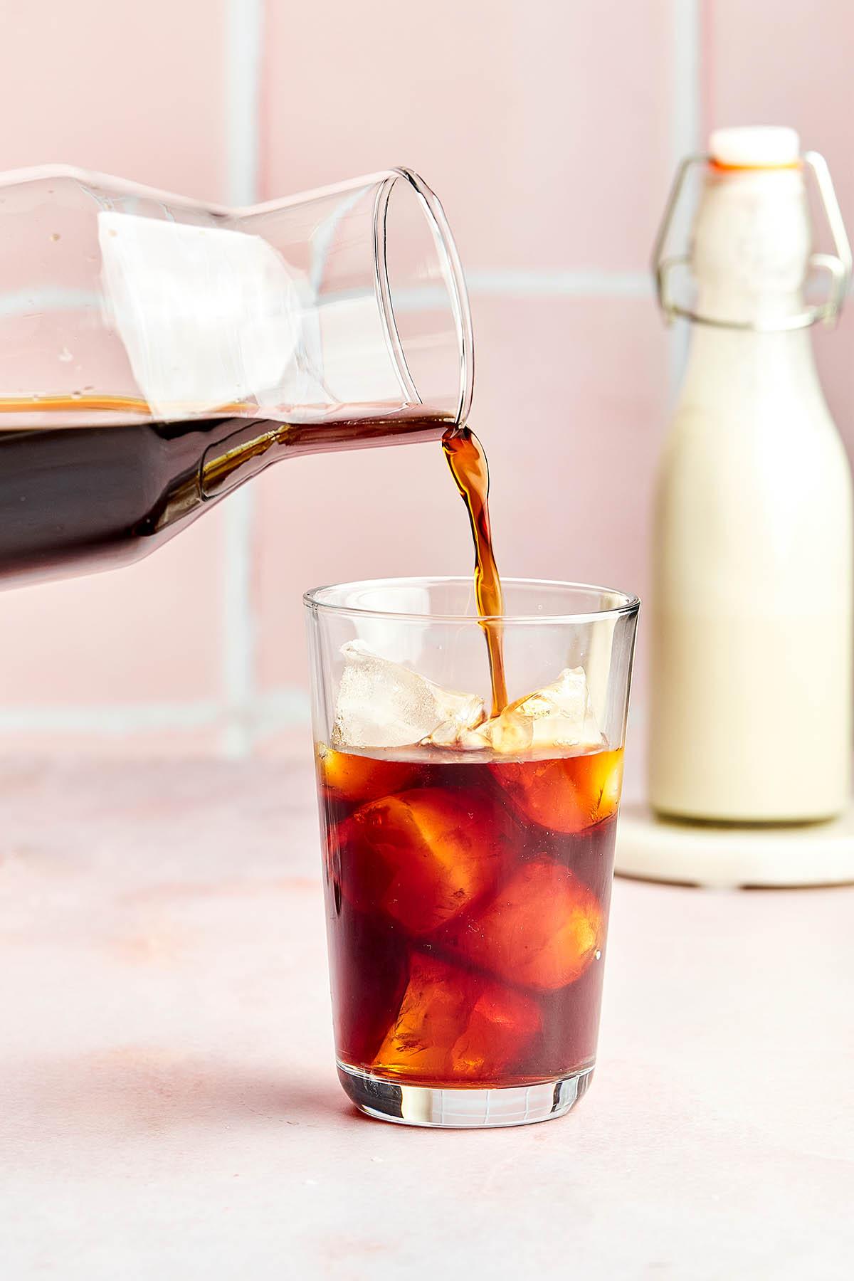 cold brew coffee being poured over ice into a glass