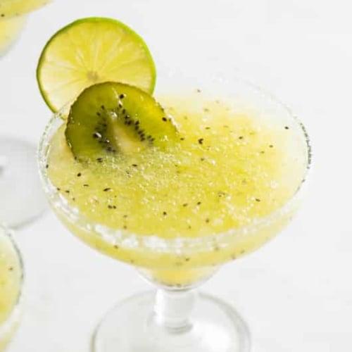 Overhead shot of several kiwi margaritas on a table with fresh kiwis and limes