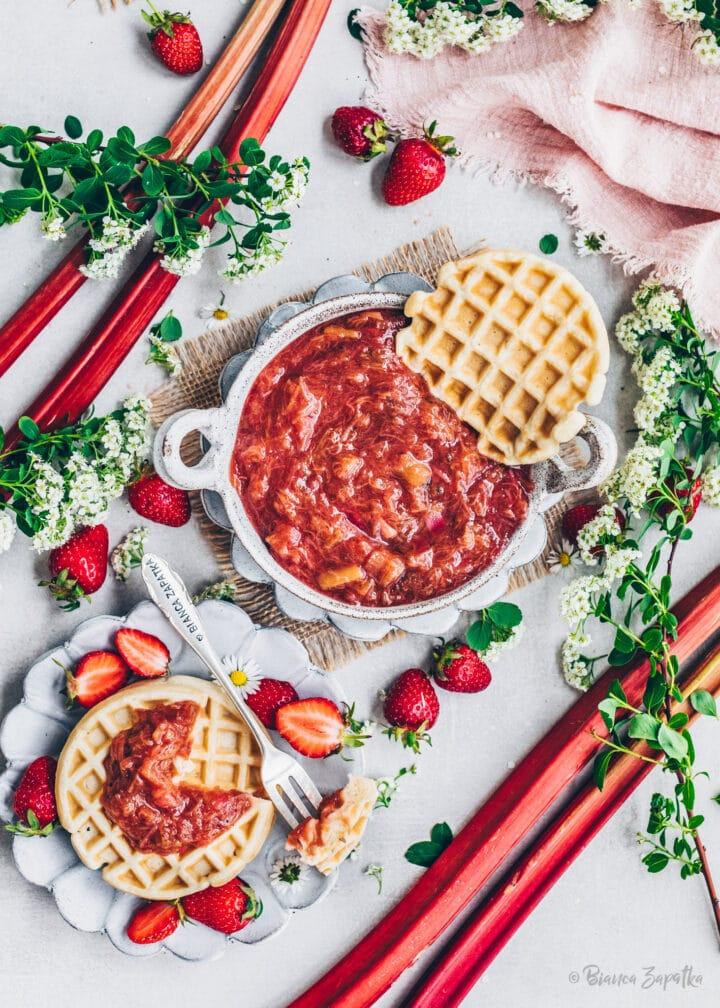 hands stirring gingerbread rhubarb compote in a pot, with holiday decorations in the background