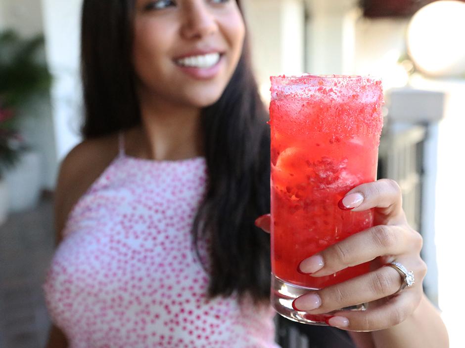 A woman smiling as she takes a sip of raspberry lassi.