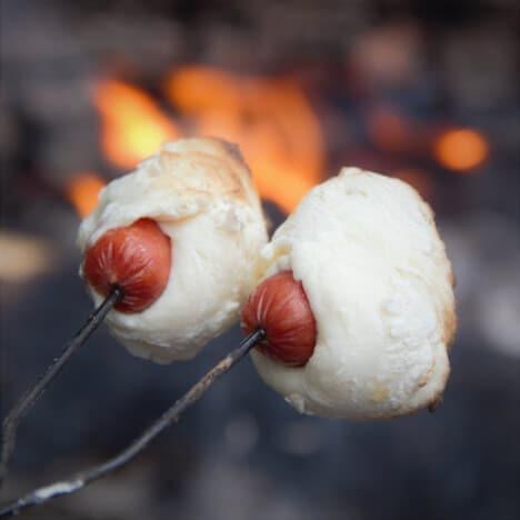 Campfire with sausages wrapped in dough cooking over it