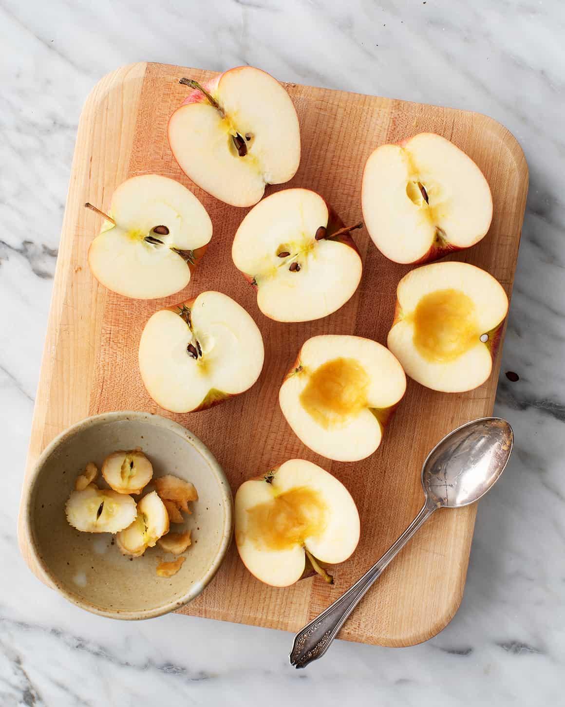 ingredients for baked apples arranged on a wooden surface: apples, cinnamon, brown sugar, butter