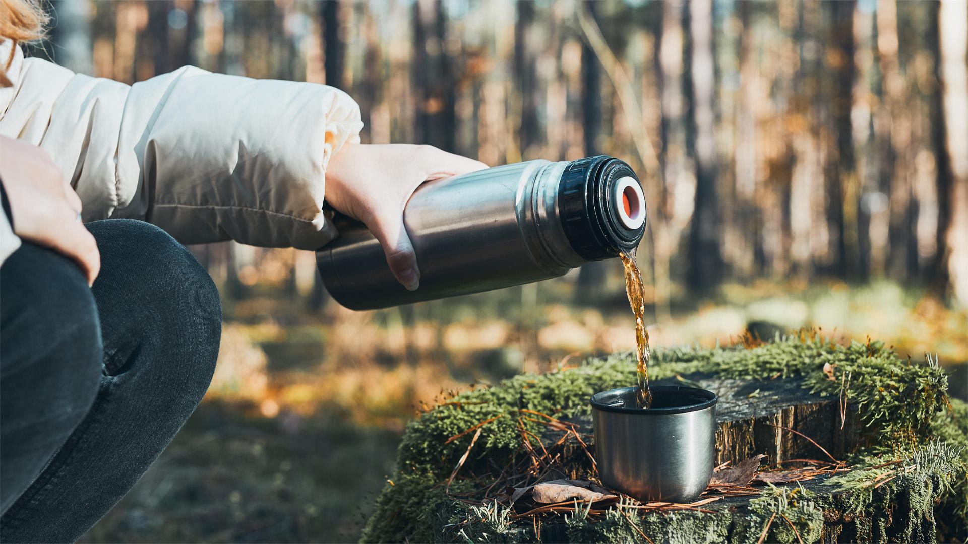 Thermos pouring cucumber mint refresher into glasses on a hiking trail