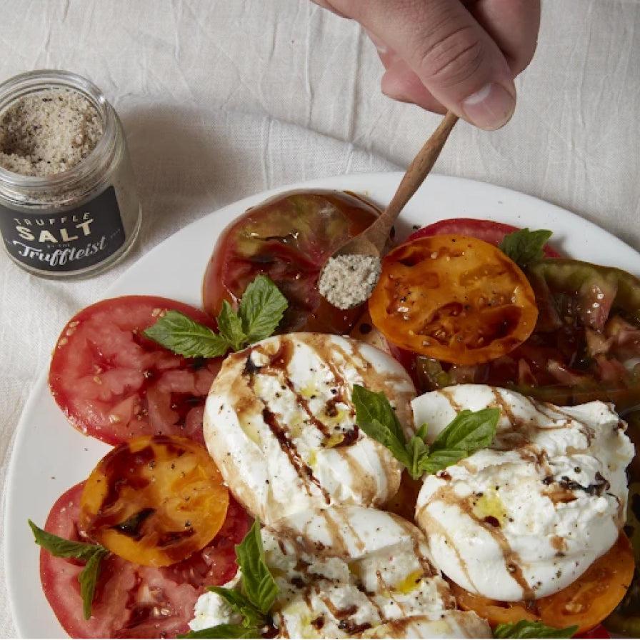 A hand drizzling truffle oil over a Truffle Infused Caprese salad