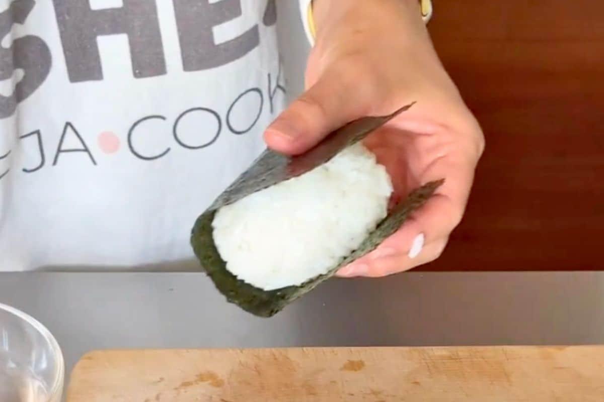 A person holding an Umeboshi and Seaweed Chicken Quinoa Onigiri, ready to take a bite