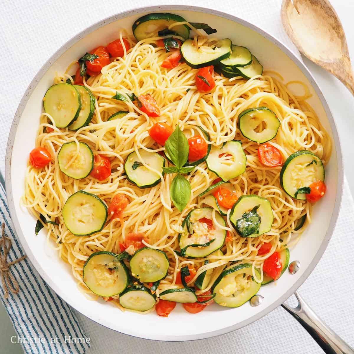 chef tossing zucchini noodles with tomatoes and basil in a pan