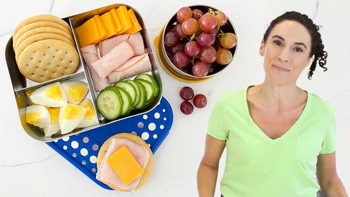 Overhead shot of a person arranging cheese slices and crackers in a bento box