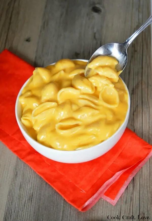 A close-up shot of creamy mac and cheese being stirred in a mug, showing the cheese melting and blending with the pasta
