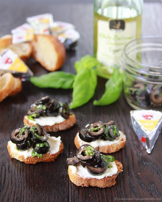 Close-up of hands reaching for olive tapenade crostini with a glass of white wine in the background