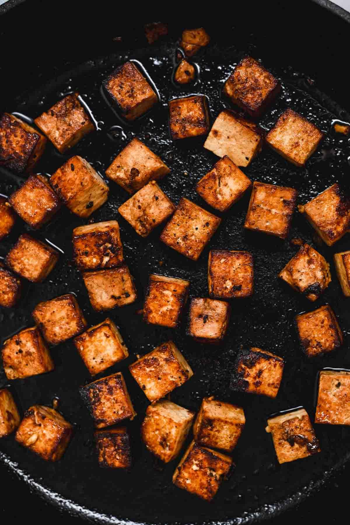 Close-up of marinated tofu slices being pan-fried