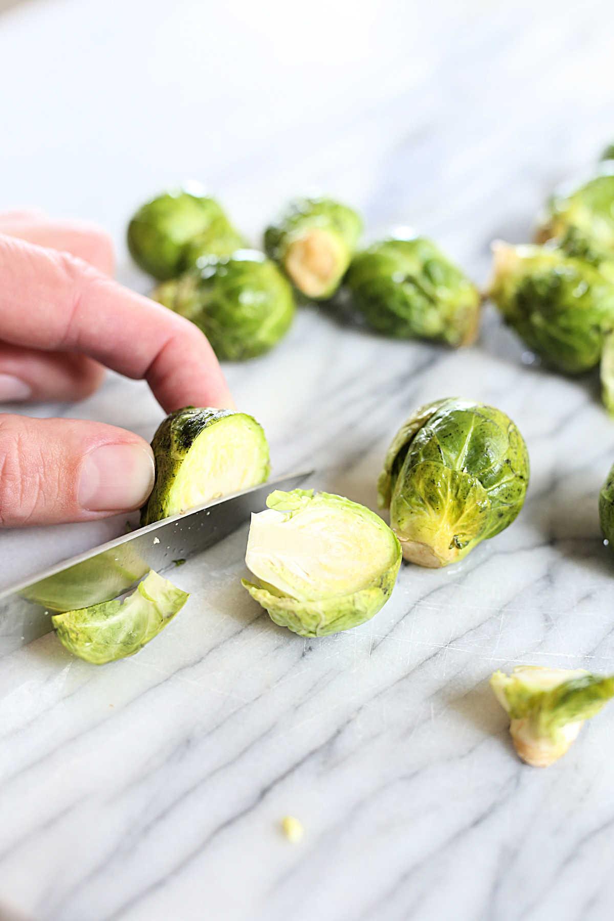 raw brussels sprouts being trimmed and halved on a cutting board