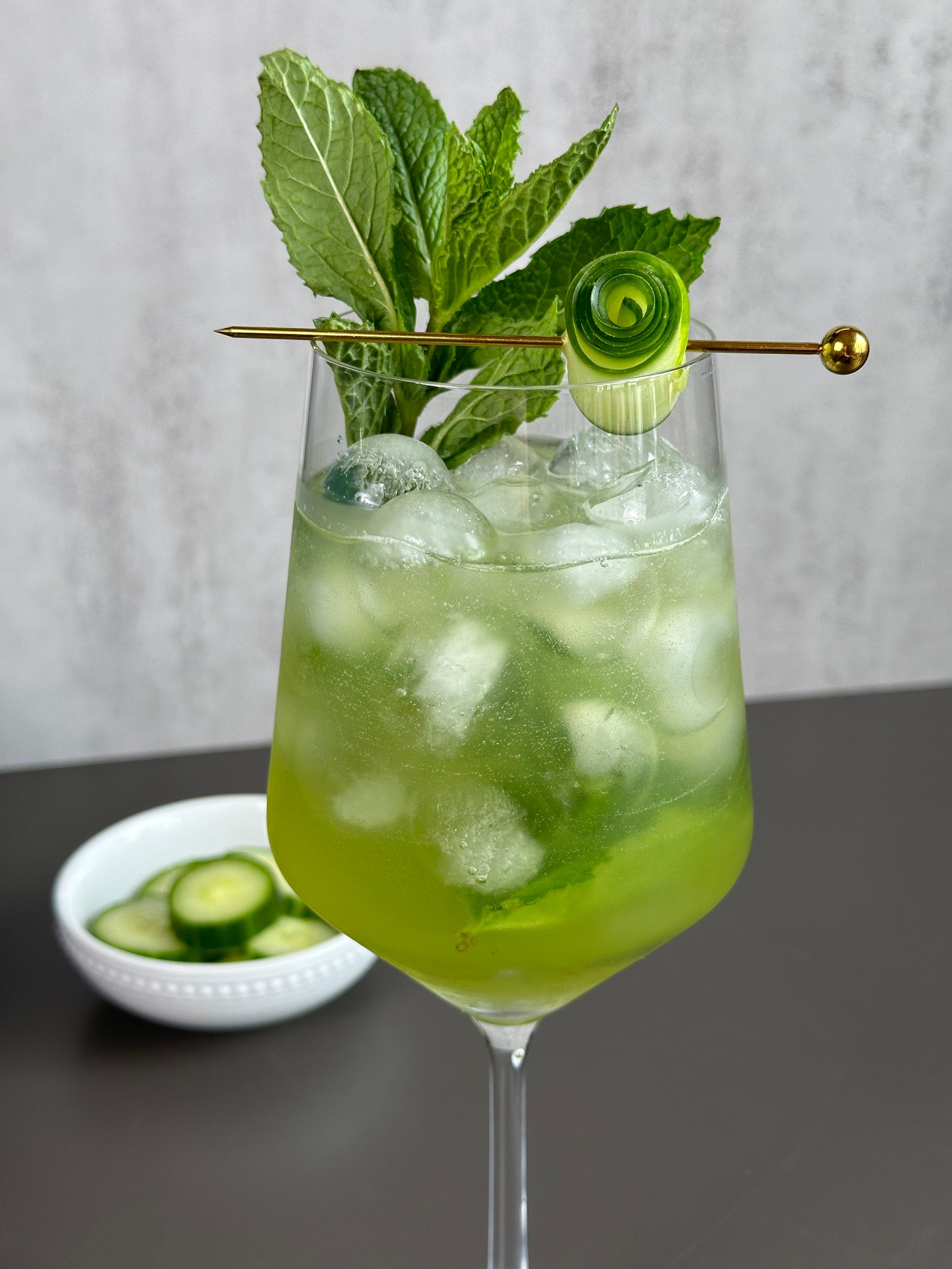 a refreshing Cucumber Melon Hugo Fizz in a highball glass with cucumber ribbons and mint sprigs