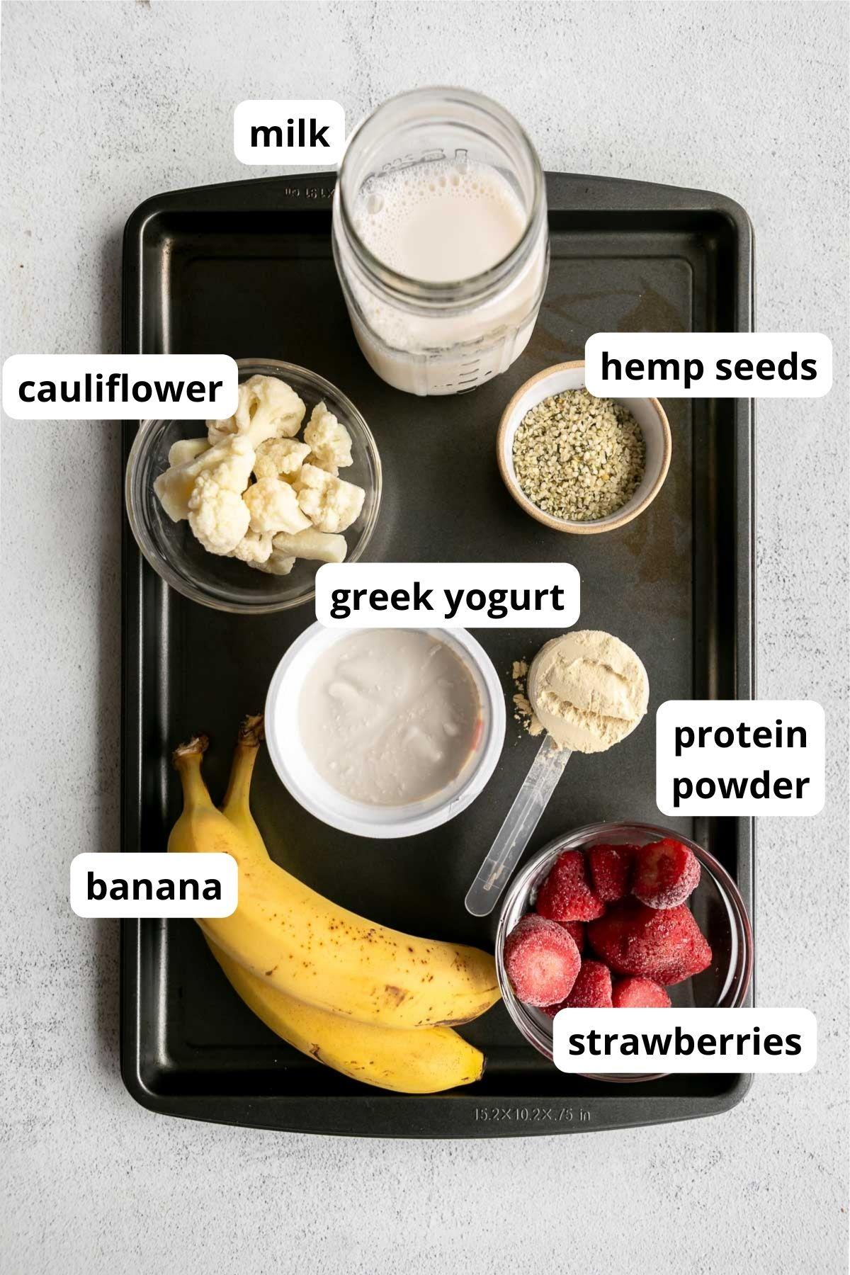 a close up shot of the ingredients: fresh strawberries, a banana, protein powder, and milk, all arranged nicely on a wooden countertop