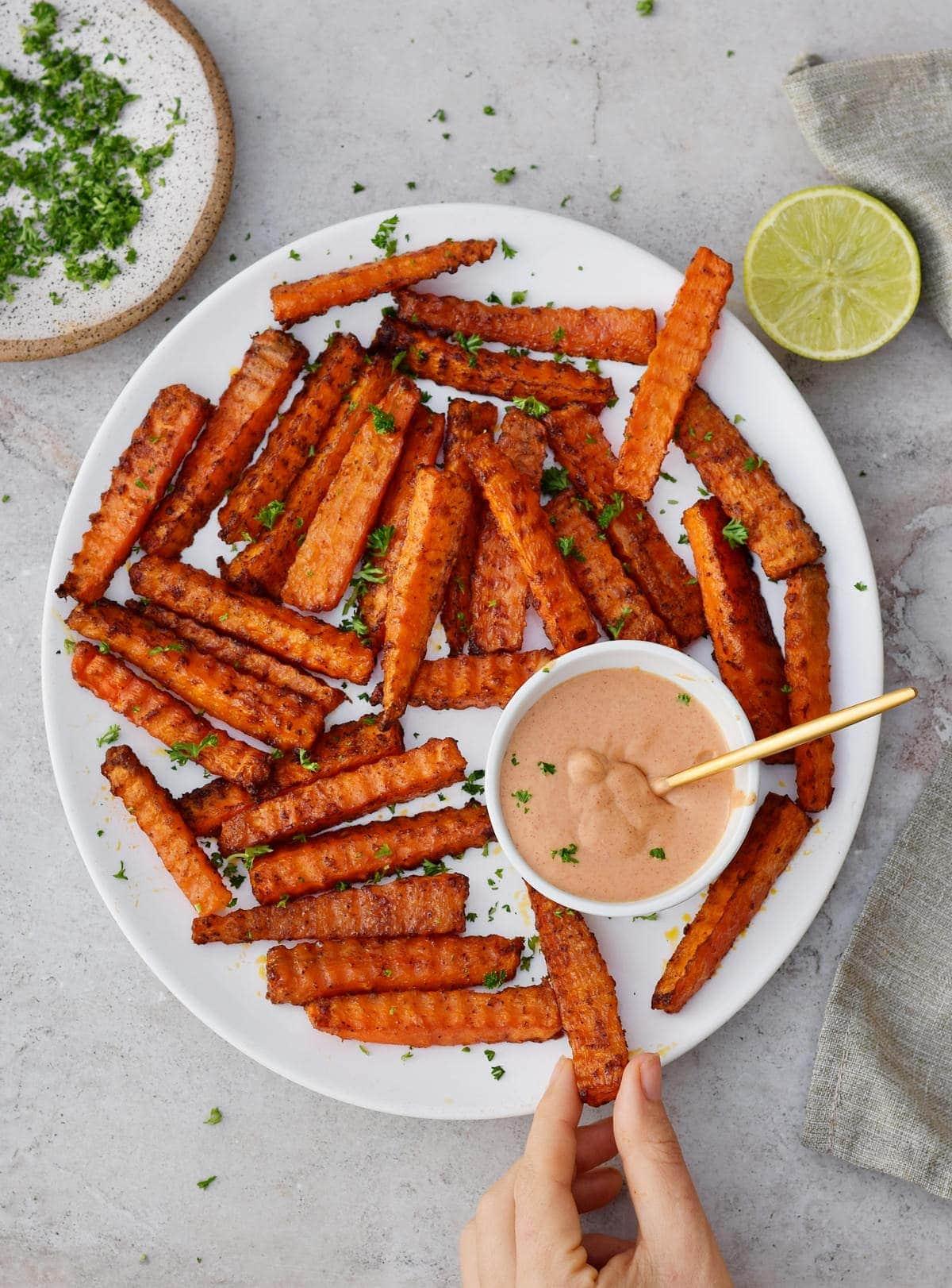 a hand reaching for ginger sesame carrot fries