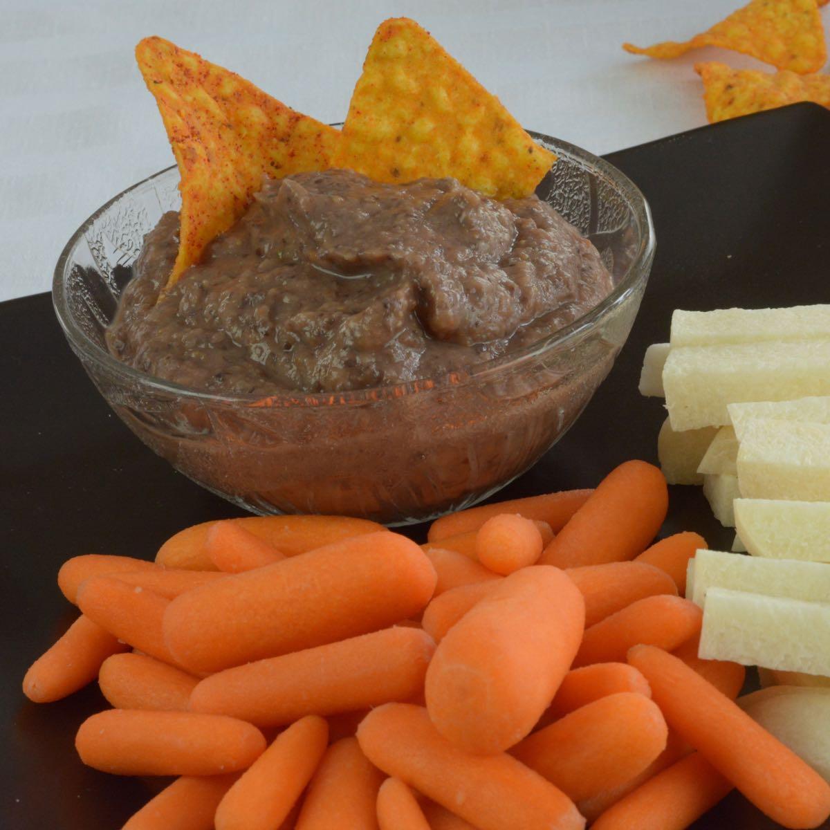 a bowl of black bean dip with carrot fries around it