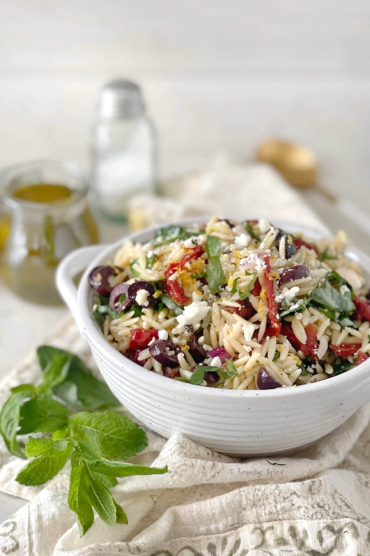 Close-up shot of a bowl of orzo pasta salad, highlighting the textures of the orzo, sun-dried tomatoes, and spinach