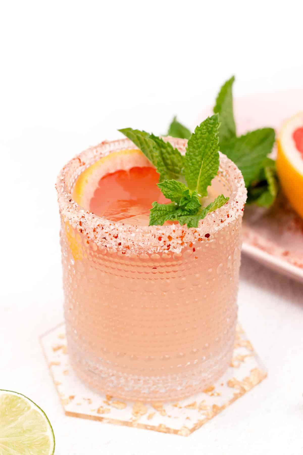 A refreshing pink cocktail with a salt rim, garnished with citrus and mint