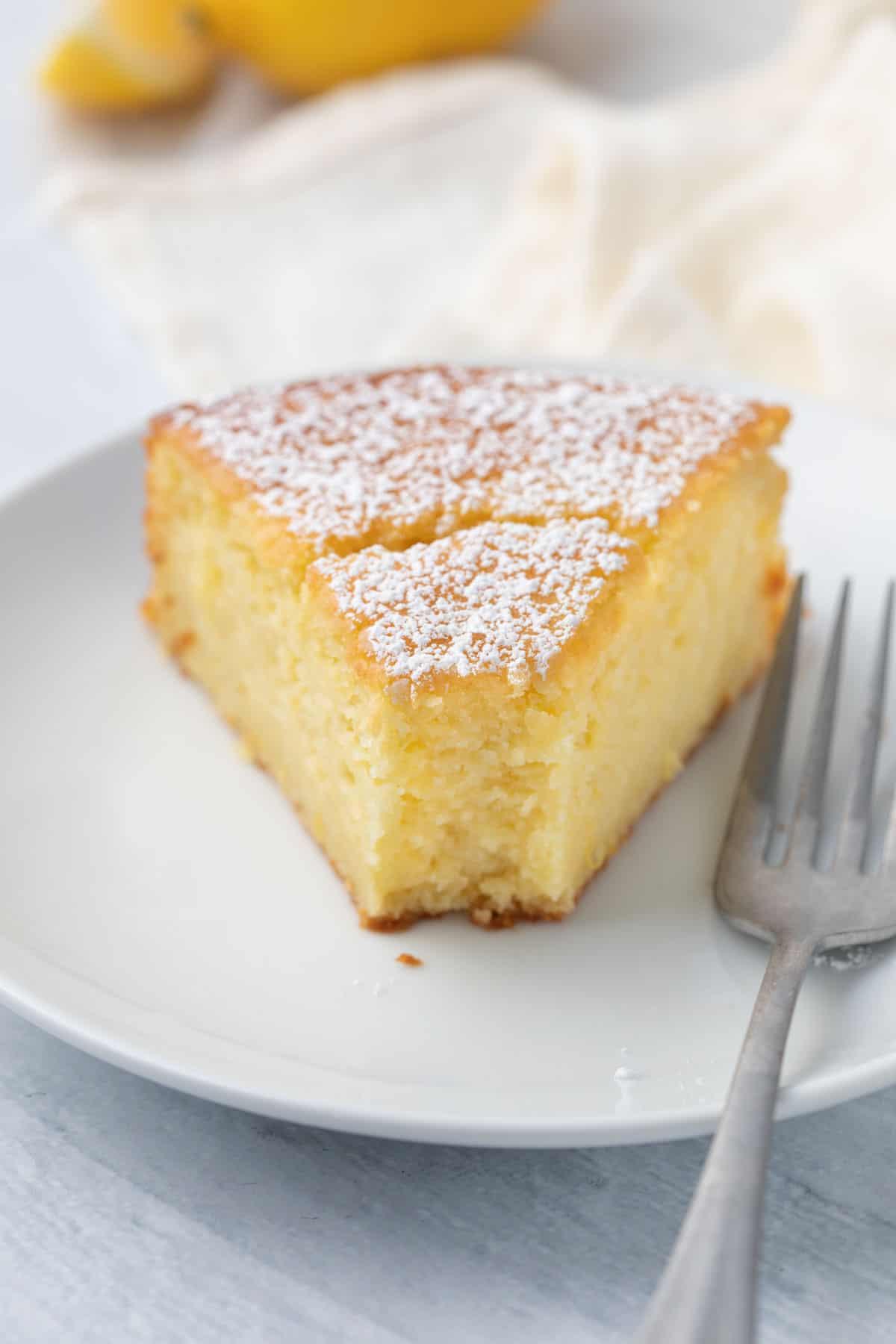 a slice of lemon ricotta cake on a plate, with a fork resting beside it