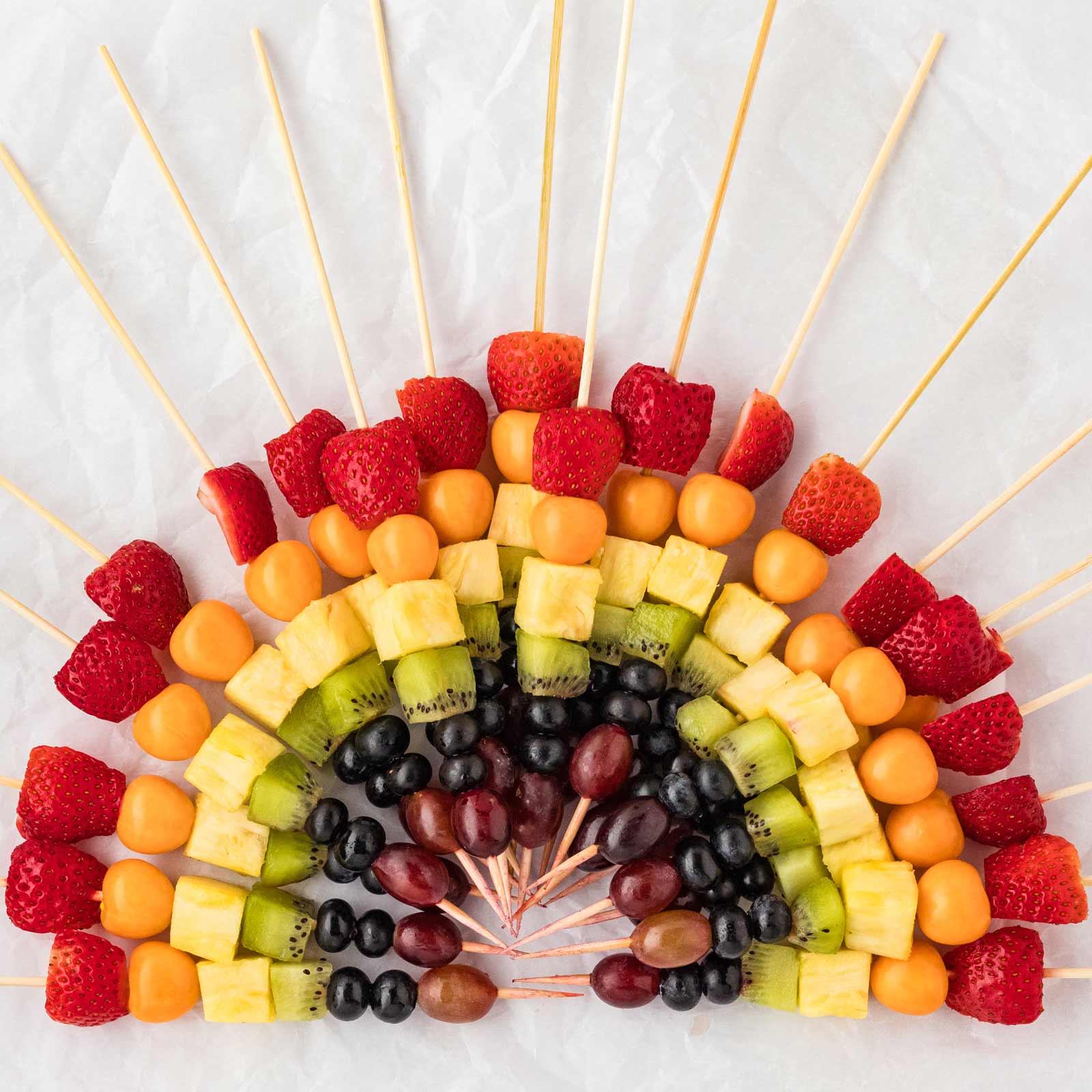 a platter of rainbow fruit skewers at a summer party