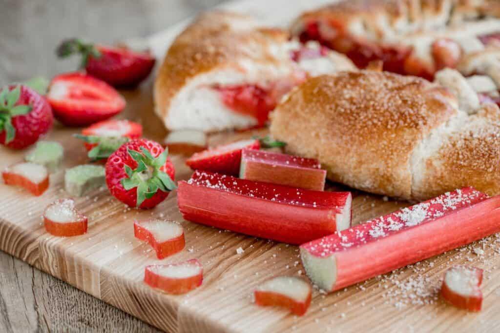 slices of Rhubarb & Fruit Loop Bread on a wooden cutting board with fresh rhubarb stalks in the background