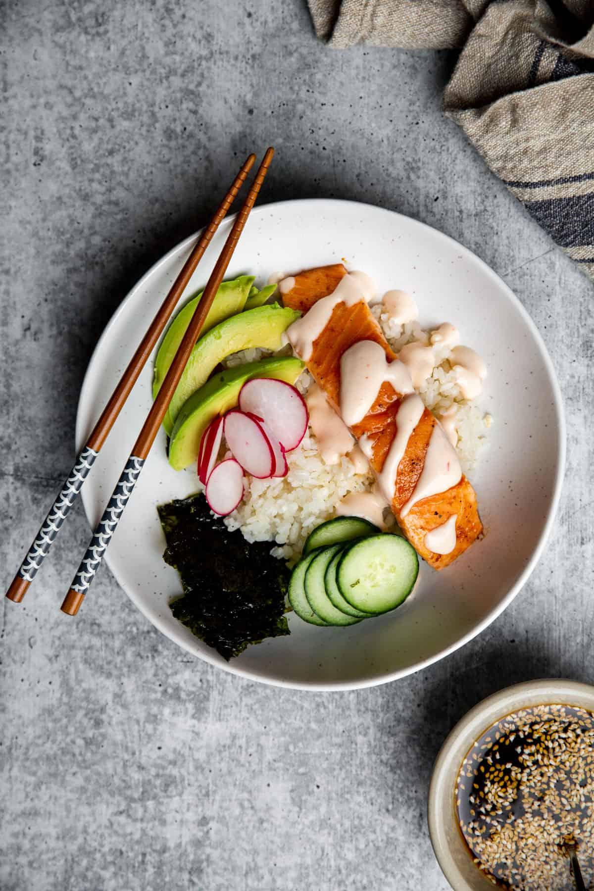 overhead shot of a sushi bowl with seasoned rice, salmon, avocado, and sesame seeds