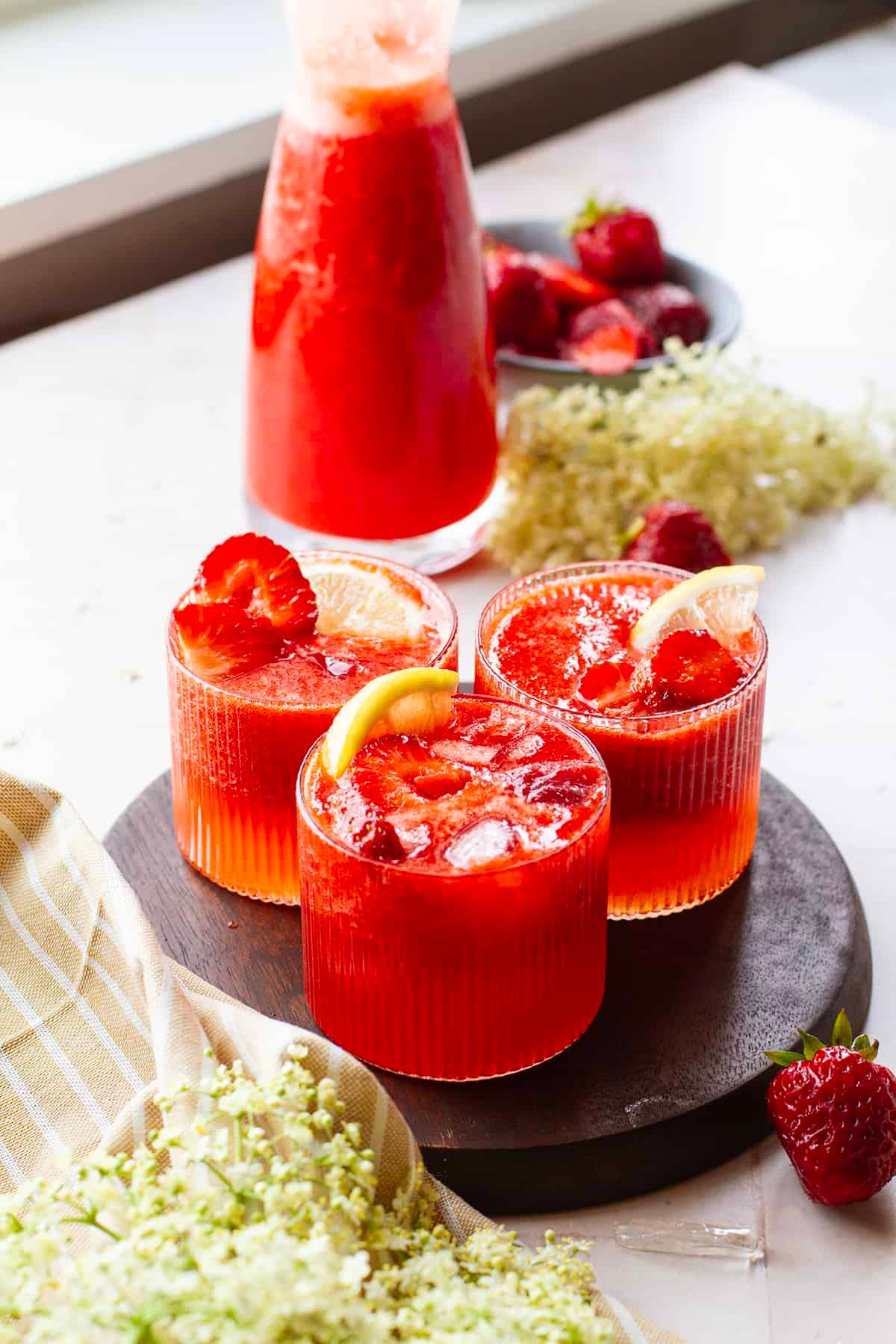 close up of a glass of strawberry elderflower lemonade with ice and condensation