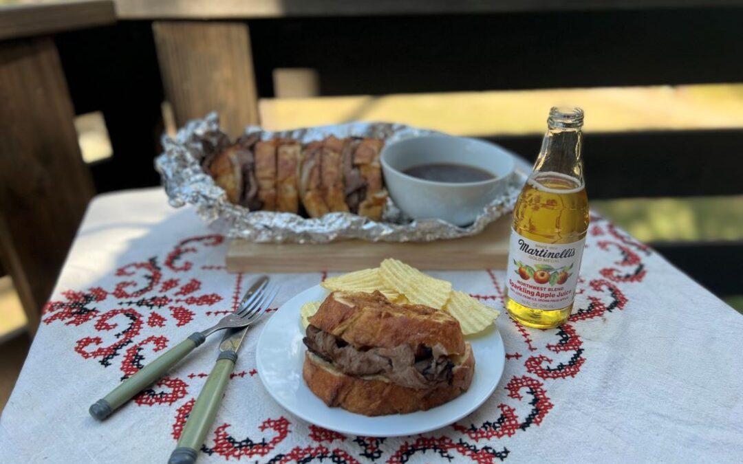 a group of people enjoying french dip sandwiches around a campfire