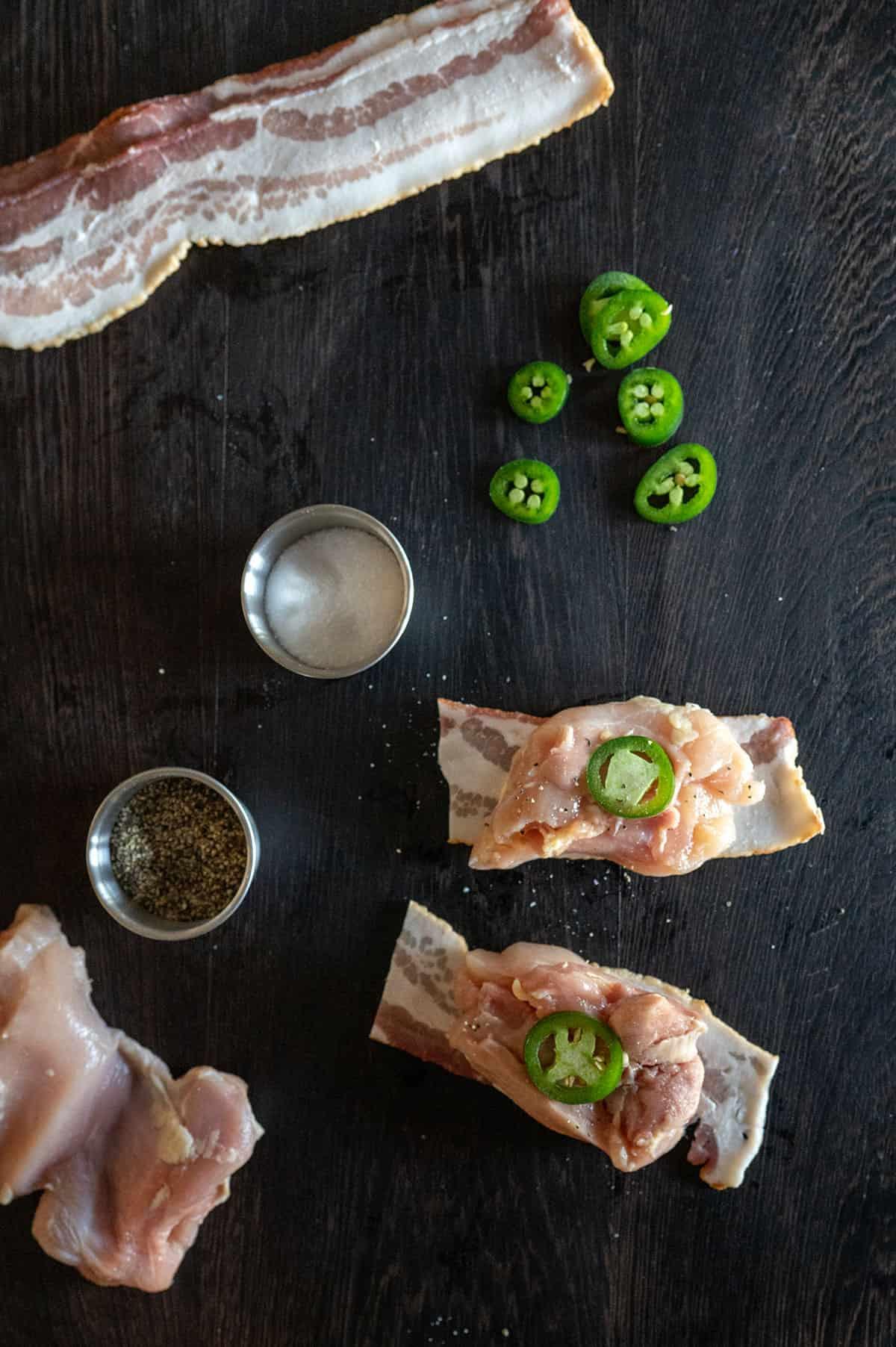 raw chicken thighs being wrapped in bacon on a cutting board