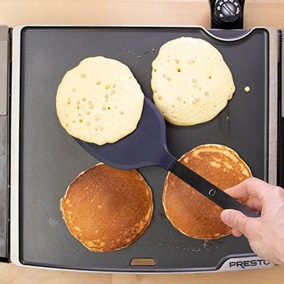 Close-up of golden brown gluten-free cornmeal pancakes being flipped on a griddle