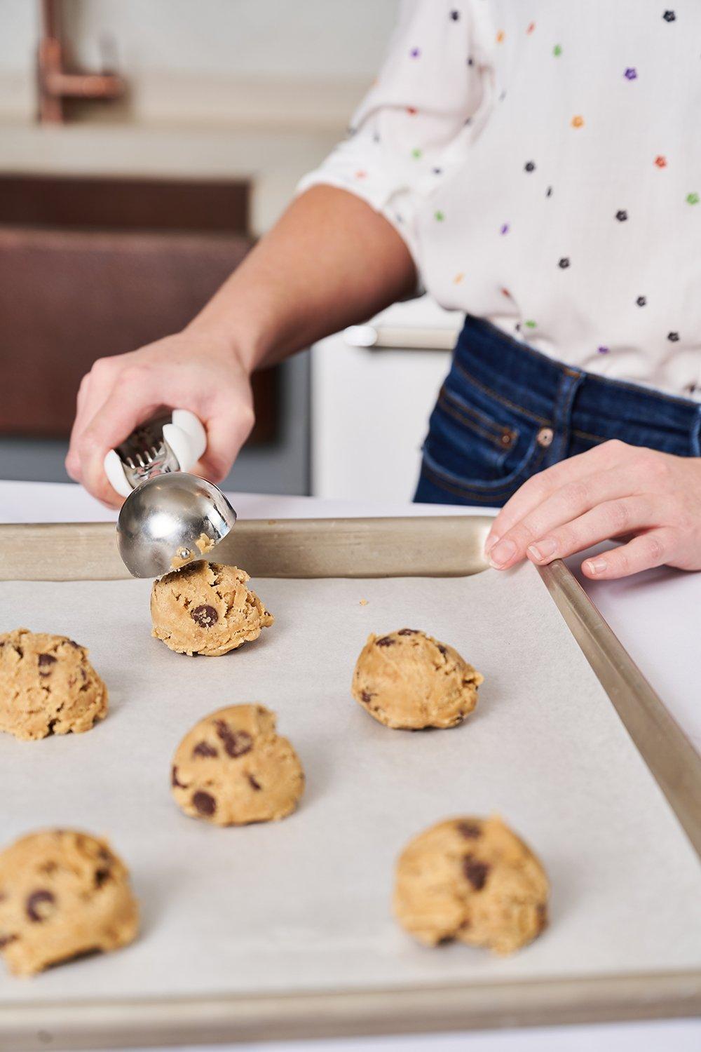 a person scooping cookie dough onto a baking sheet