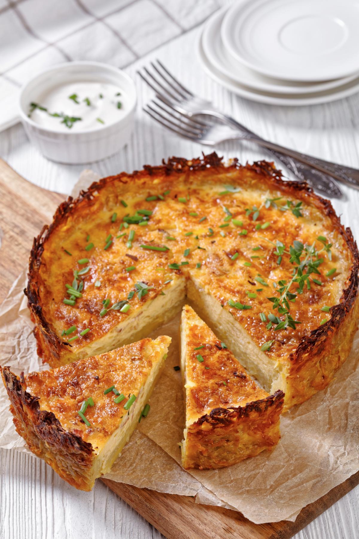 a hand sprinkling shredded Gruyère cheese over the vegetable filling in the quiche