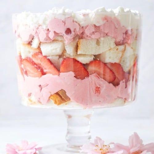 A vibrant and delicious strawberry trifle displayed in a glass trifle dish, showcasing layers of sponge cake, custard, strawberries, and whipped cream