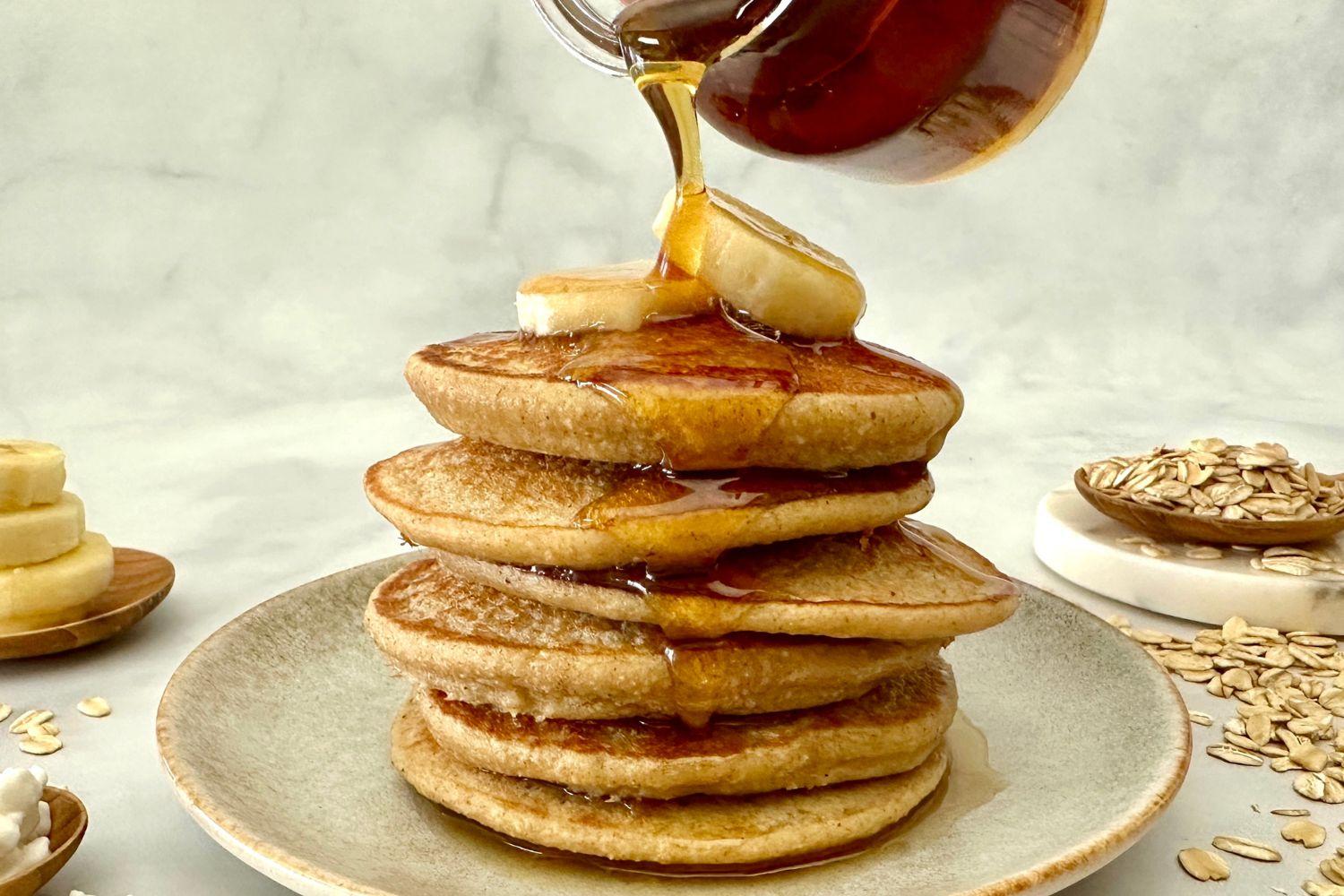 overhead shot of banana bread cottage cheese pancakes on a plate being drizzled with maple syrup