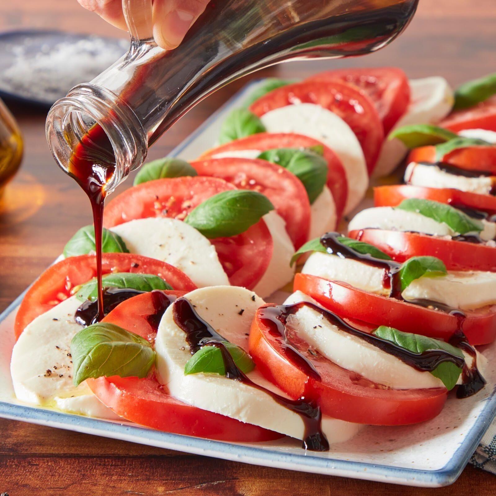 Ingredients for caprese salad, including tomatoes, mozzarella, basil, and white balsamic vinegar