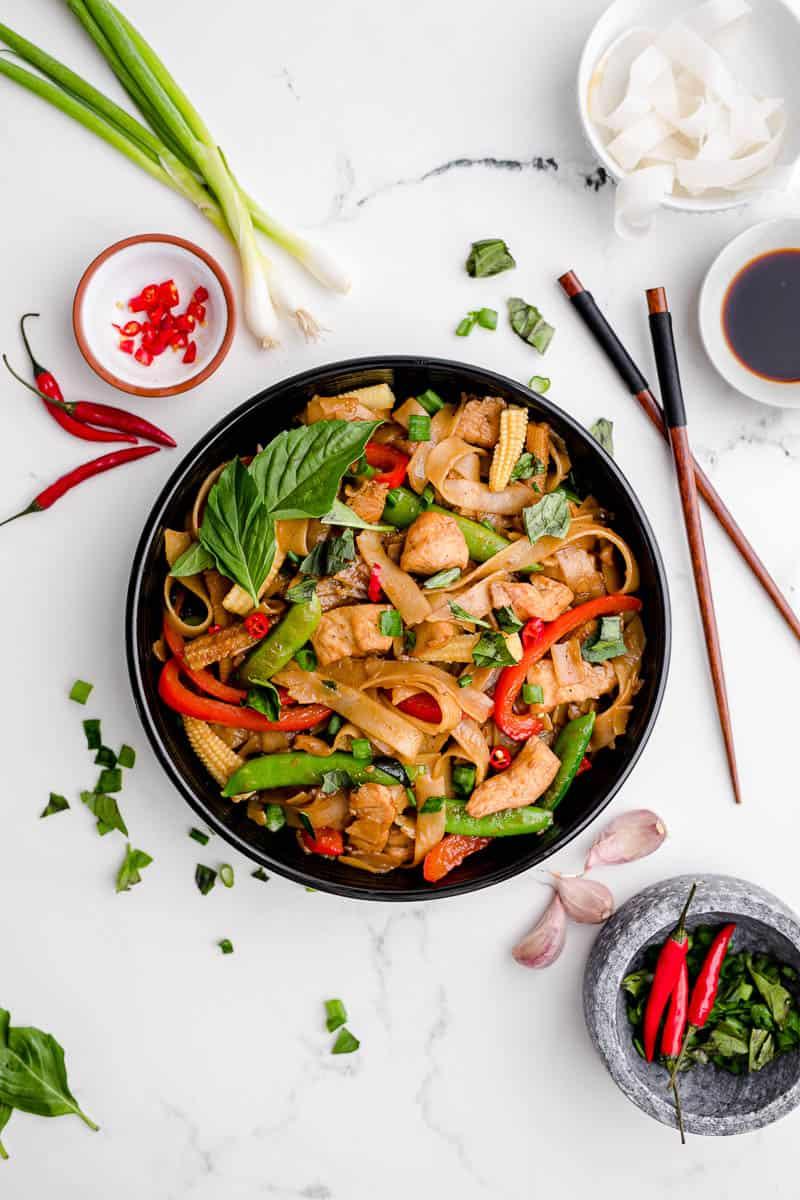 overhead shot of a table setting with drunken noodles chicken stir-fry, chopsticks, and a glass of iced tea