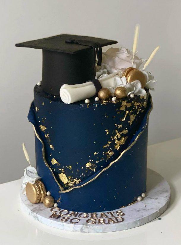 A beautifully decorated blue and gold graduation cake on a table with graduation decorations