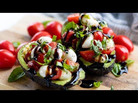 A person holding a Caprese stuffed avocado over a campfire, with the fire slightly blurred in the background