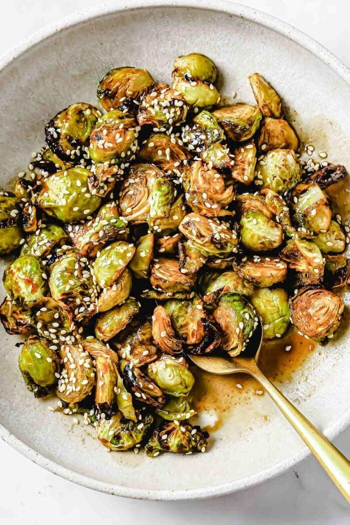 a close-up shot of roasted brussels sprouts being tossed in a bowl with sesame seeds and rice vinegar