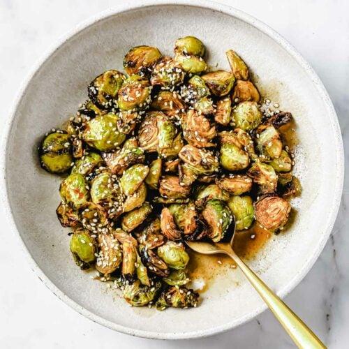overhead shot of black garlic roasted brussels sprouts arranged on a serving platter with sesame seeds sprinkled on top