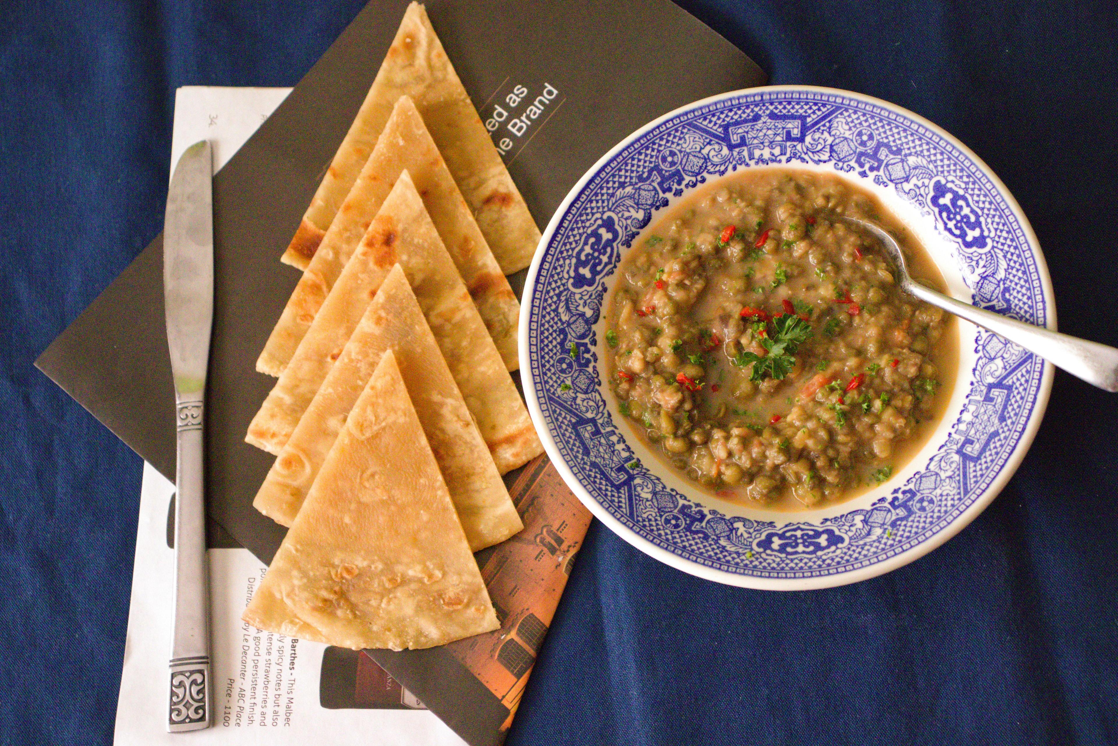overhead shot of lentil soup, bread, and butter on a wooden table