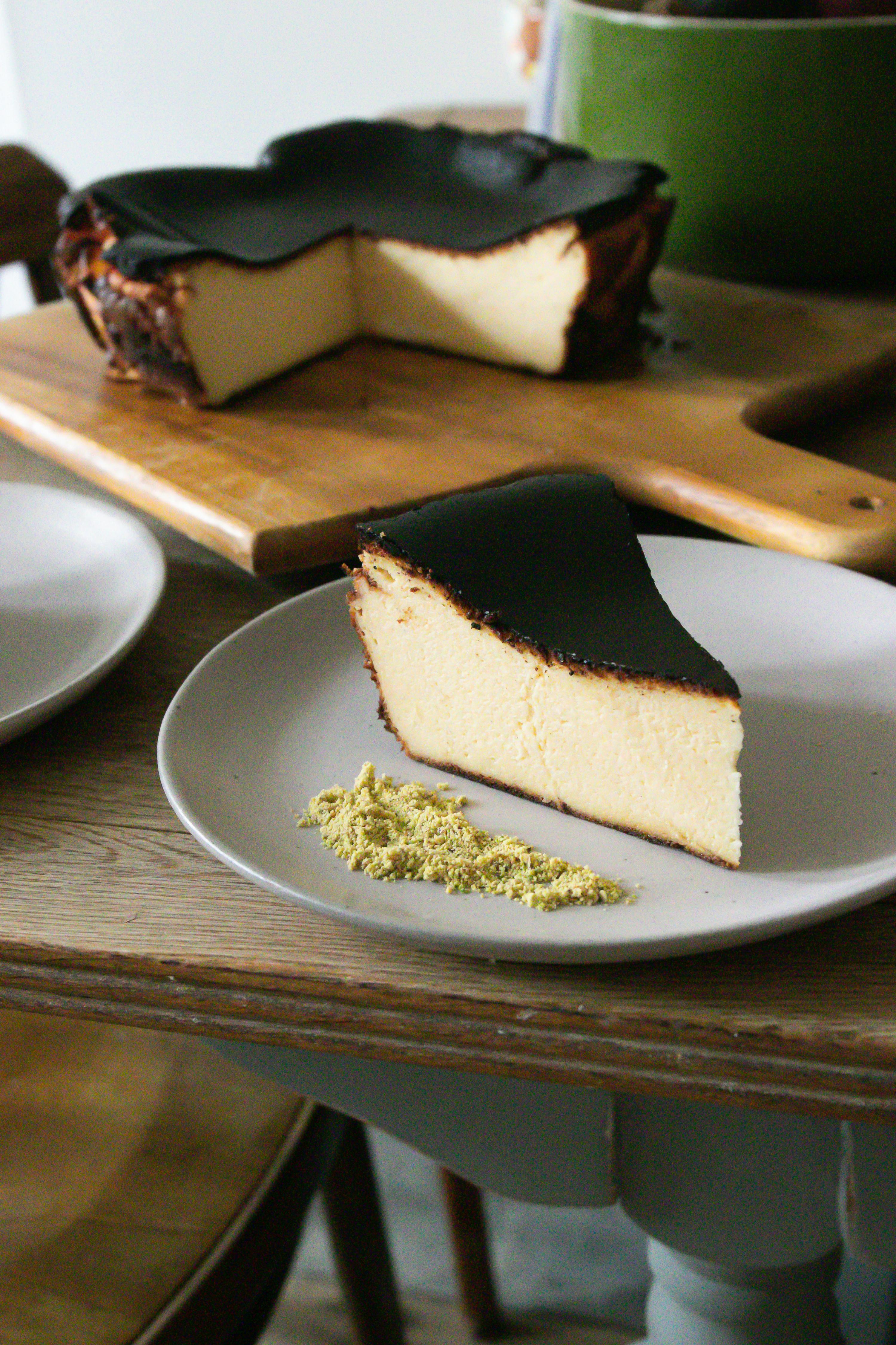 Overhead shot of a whole Basque Burnt Cheesecake on a wooden table, with a knife and serving utensils nearby