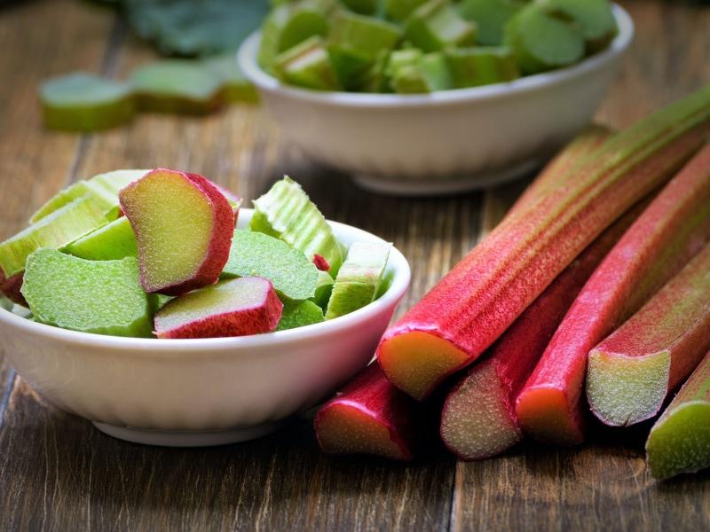 fresh rhubarb stalks and sliced kiwis on a wooden cutting board